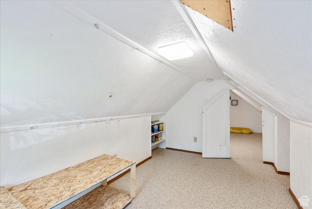 Bonus room with a textured ceiling, lofted ceiling, and light colored carpet