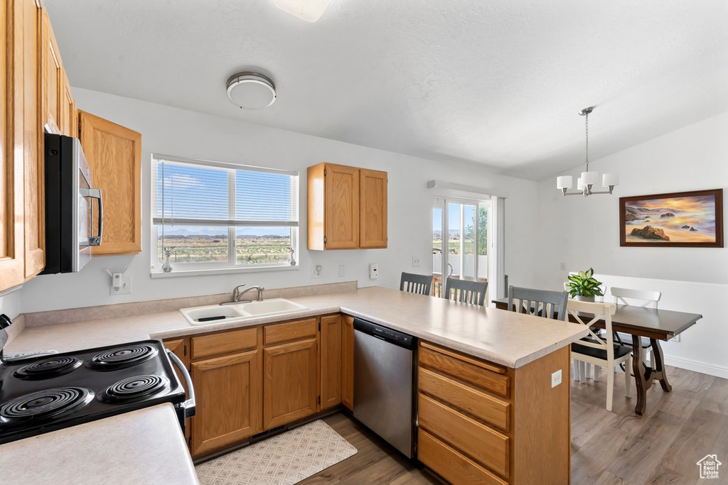 Kitchen with stainless steel appliances, a peninsula, light wood-style flooring, a chandelier, and light countertops