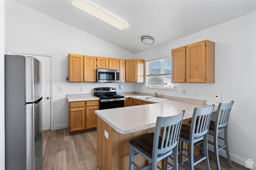Kitchen with stainless steel appliances, lofted ceiling, a peninsula, light countertops, and light wood-type flooring