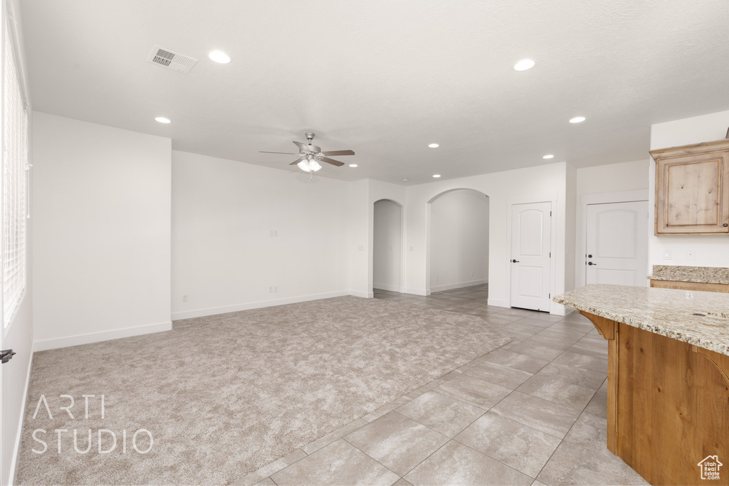 Unfurnished living room featuring arched walkways, recessed lighting, ceiling fan, light tile patterned flooring, and light colored carpet