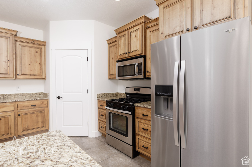 Kitchen with appliances with stainless steel finishes, light stone countertops, and light tile patterned flooring
