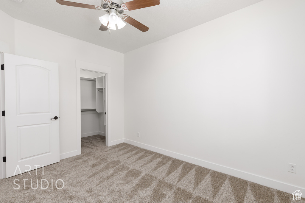 Unfurnished bedroom with carpet, a spacious closet, ceiling fan, and a closet