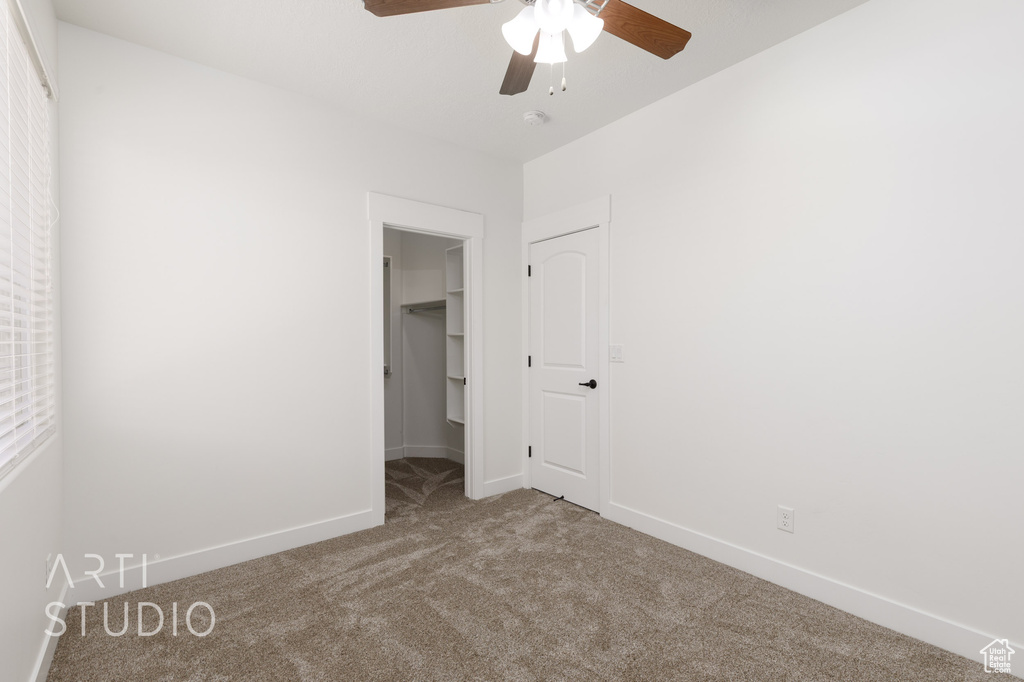 Unfurnished bedroom featuring carpet floors, a spacious closet, a ceiling fan, and a closet