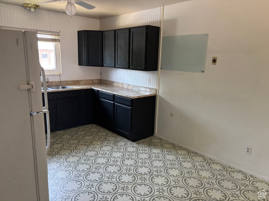 Kitchen featuring freestanding refrigerator, light countertops, ceiling fan, and dark cabinetry