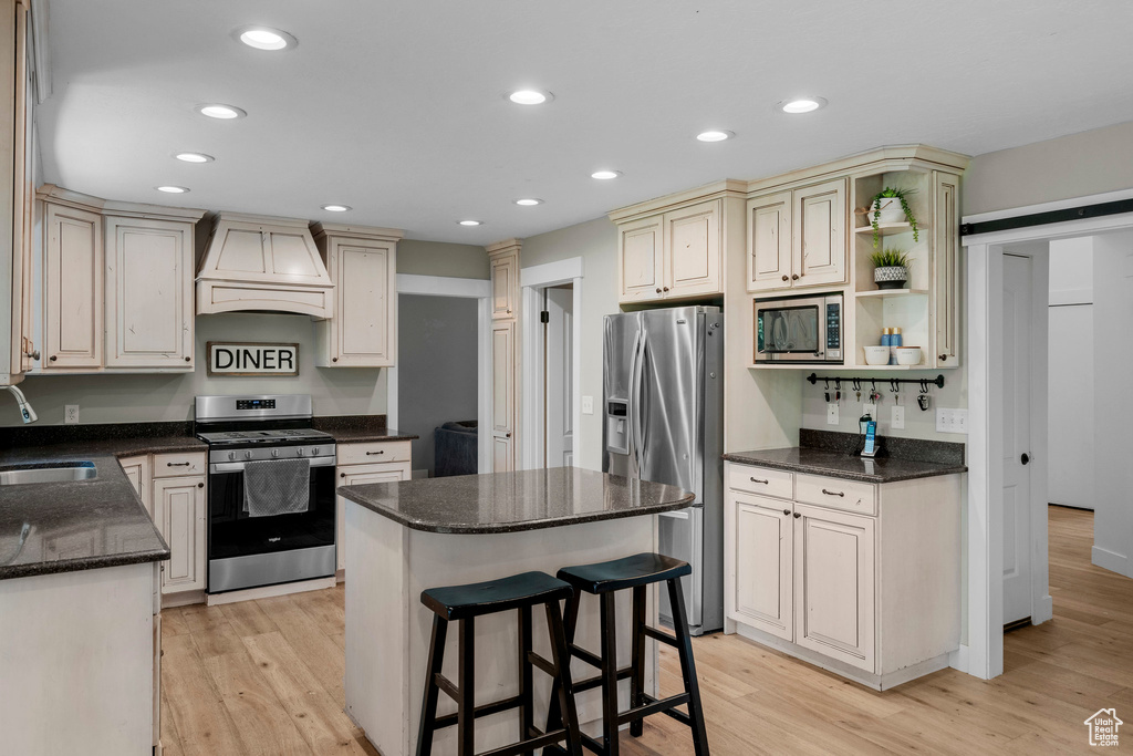 Kitchen with stainless steel appliances, custom range hood, a kitchen island, recessed lighting, and light wood-style flooring