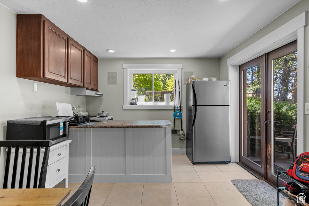 Kitchen featuring stainless steel appliances, light tile patterned floors, a peninsula, under cabinet range hood, and french doors