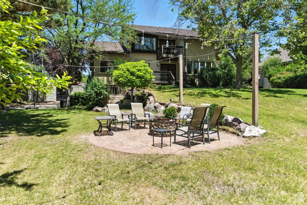 View of green lawn with a fire pit, a patio, and a balcony
