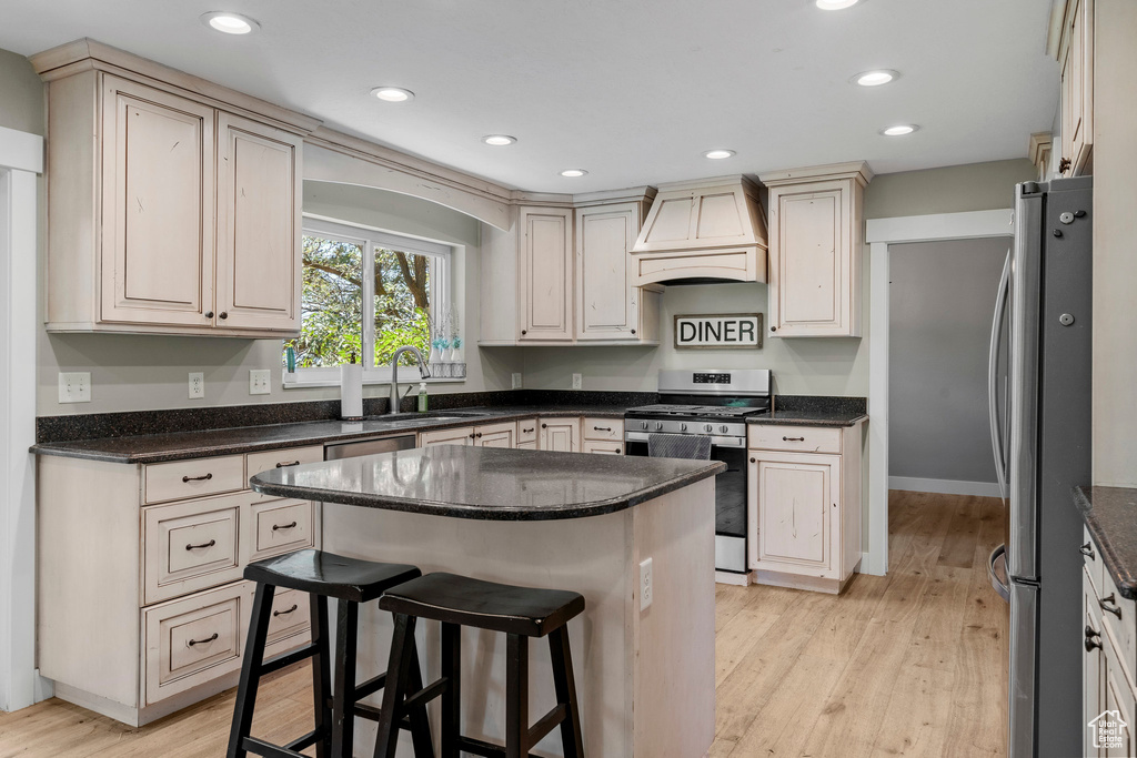 Kitchen featuring appliances with stainless steel finishes, custom exhaust hood, light wood-type flooring, recessed lighting, and a breakfast bar