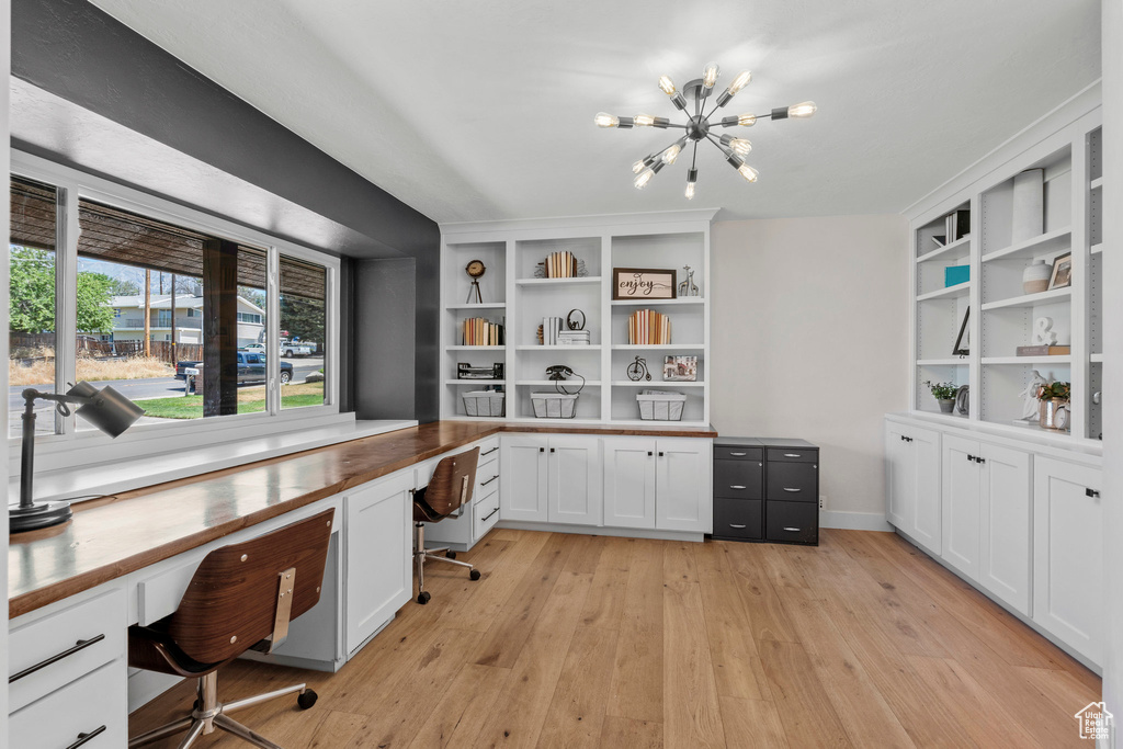 Office area with built in study area, light wood finished floors, and a chandelier