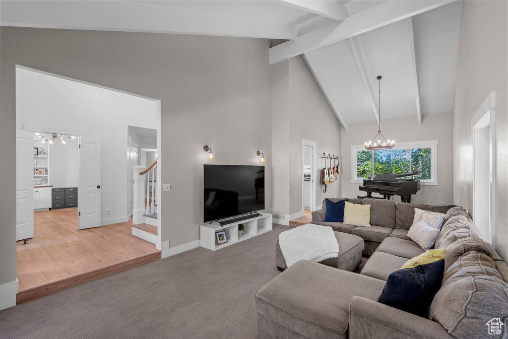 Living room with a chandelier, stairway, high vaulted ceiling, beam ceiling, and light carpet