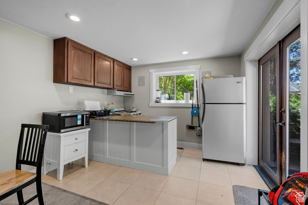 Kitchen featuring stainless steel appliances, a peninsula, light tile patterned floors, recessed lighting, and brown cabinetry