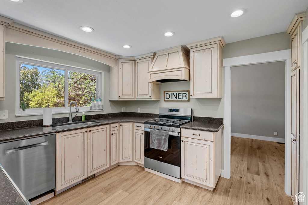 Kitchen featuring stainless steel appliances, premium range hood, cream cabinetry, light wood-style floors, and recessed lighting