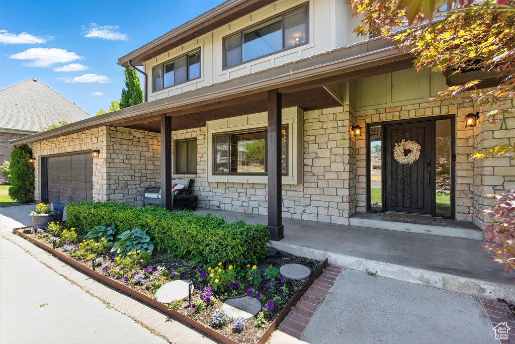 Property entrance with covered porch, stone siding, and a garage