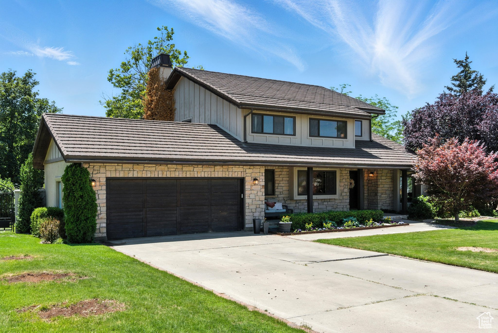 View of front facade featuring board and batten siding, a garage, a chimney, concrete driveway, and a front lawn