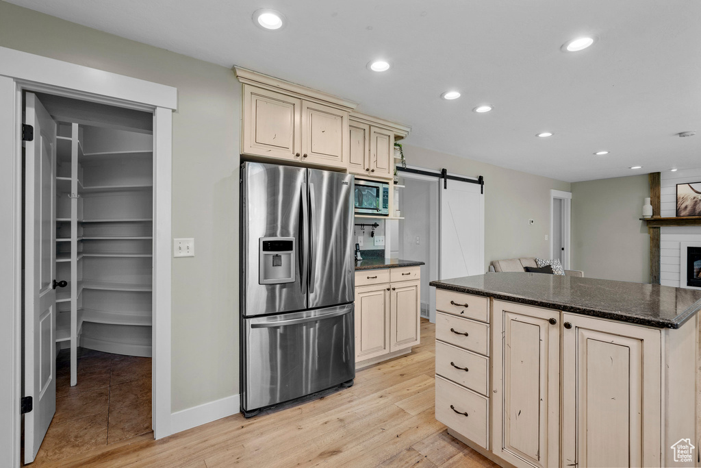 Kitchen featuring stainless steel appliances, cream cabinets, a barn door, light wood-type flooring, and recessed lighting