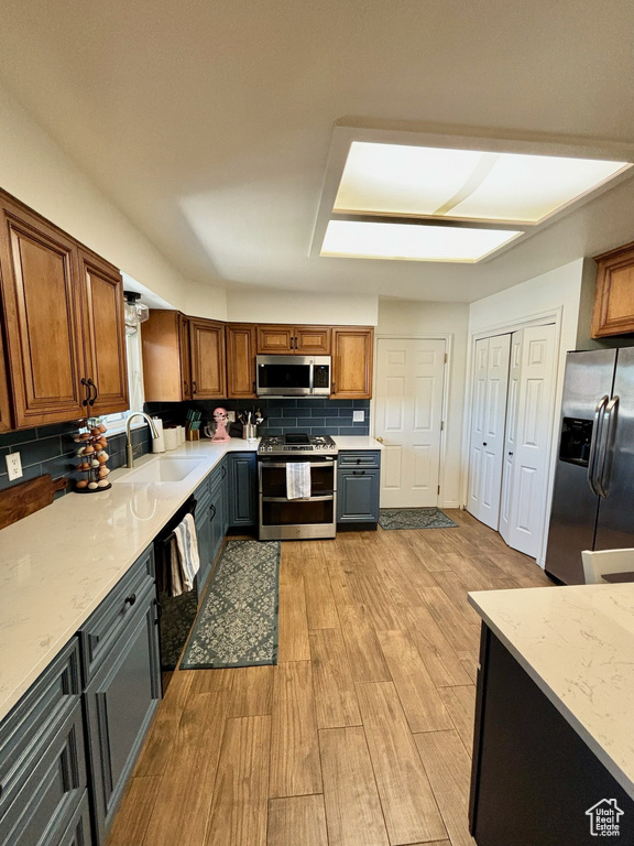 Kitchen with stainless steel appliances, light wood-style floors, decorative backsplash, and brown cabinets