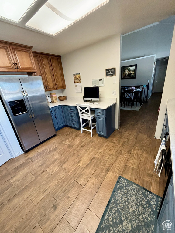 Kitchen with stainless steel fridge, light wood-type flooring, light countertops, blue cabinets, and built in desk