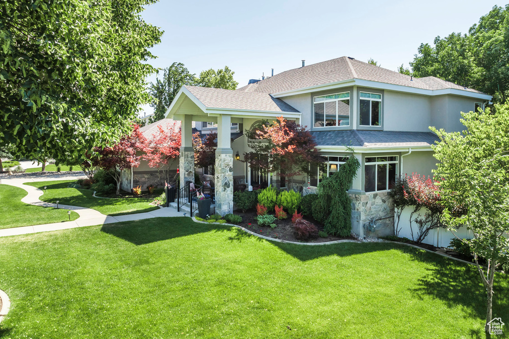 View of front facade featuring stucco siding, a front lawn, stone siding, and roof with shingles