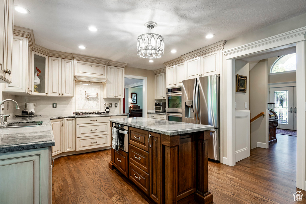 Kitchen with appliances with stainless steel finishes, dark wood finished floors, backsplash, light stone counters, and glass insert cabinets