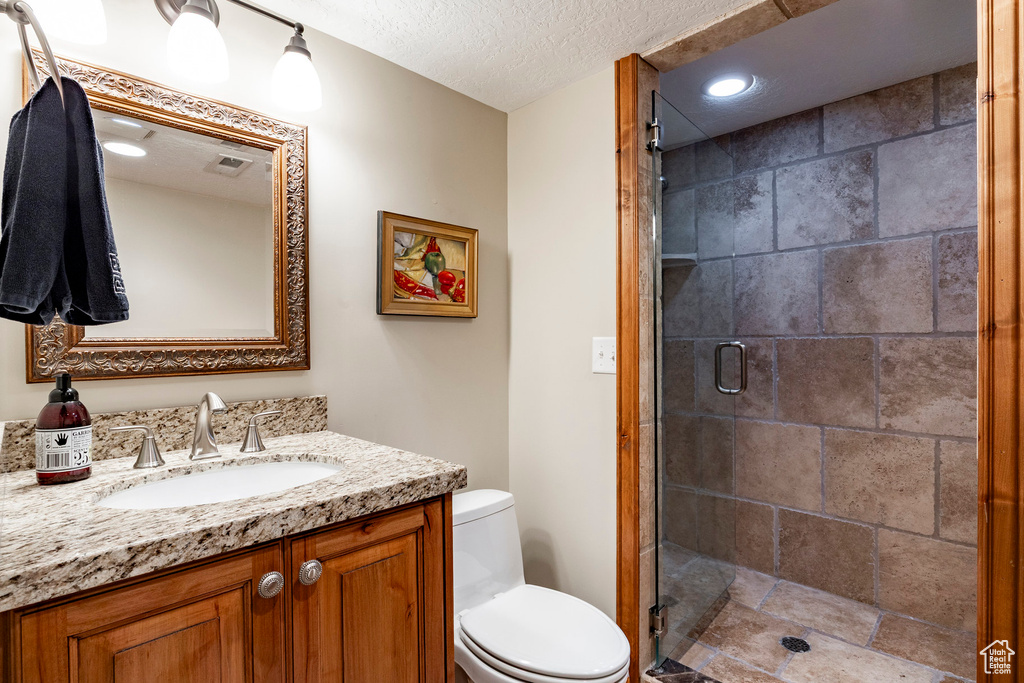 Full bath featuring vanity, a shower stall, a textured ceiling, recessed lighting, and stone finish floors