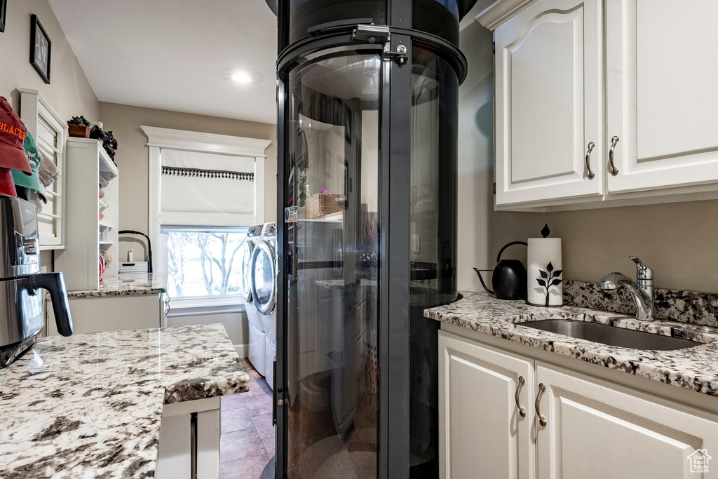 Kitchen with white cabinetry, light stone countertops, and washing machine and clothes dryer