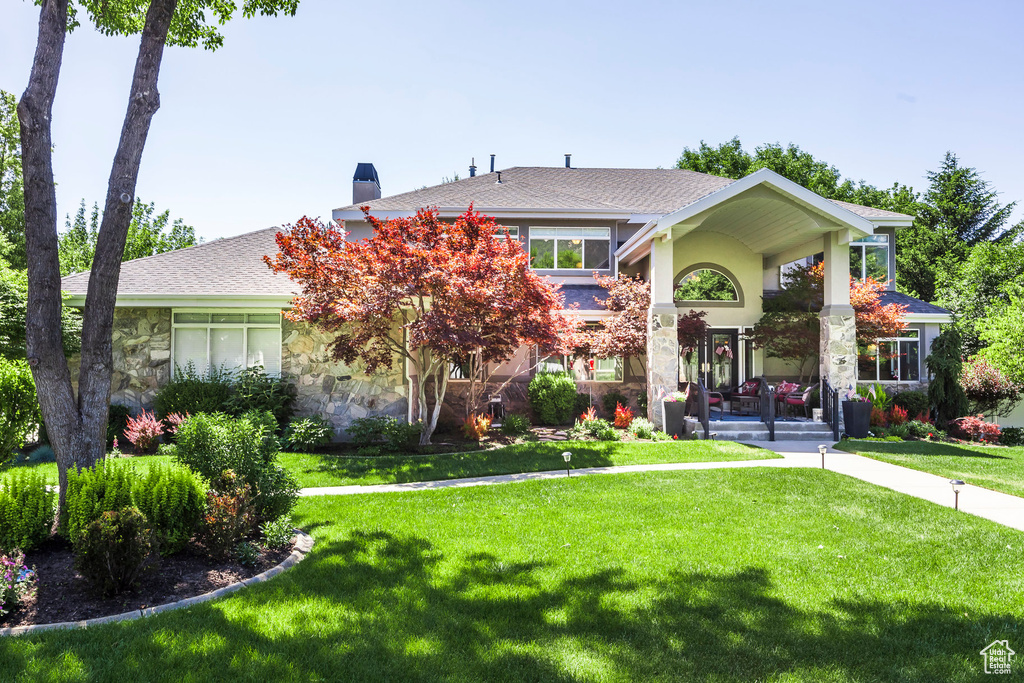 View of front of home with a chimney, stone siding, a front yard, and a shingled roof