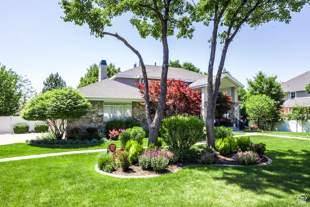 View of property hidden behind natural elements with stone siding, a chimney, and a shingled roof