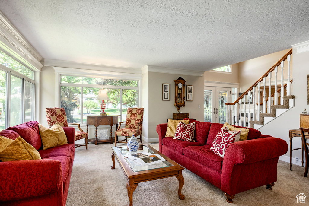Carpeted living room featuring a textured ceiling, crown molding, stairway, and french doors