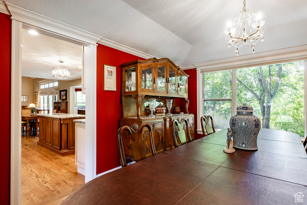 Dining space with a chandelier, light wood-style floors, ornamental molding, and vaulted ceiling