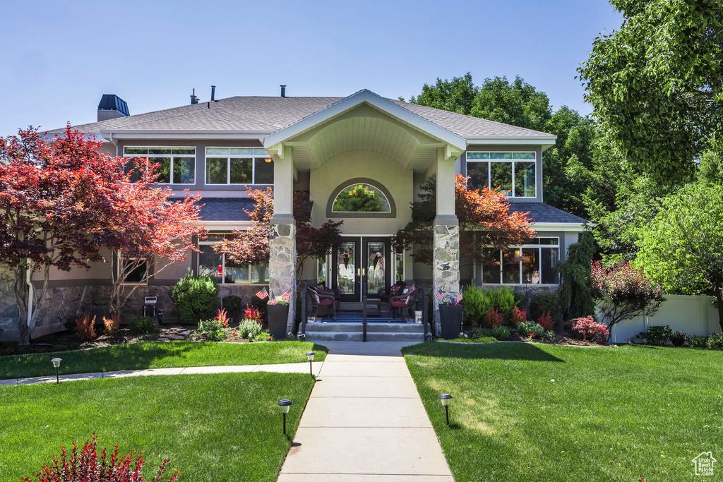 View of front of house featuring a shingled roof, a front yard, stucco siding, and a porch