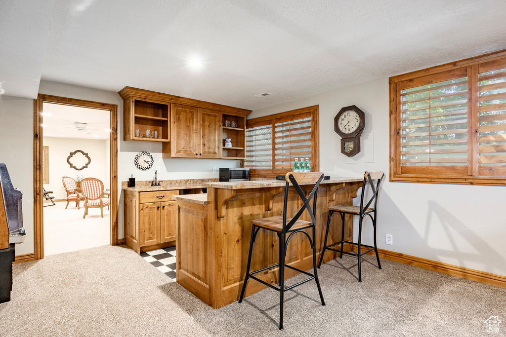Kitchen with open shelves, black microwave, a kitchen bar, light countertops, and light carpet