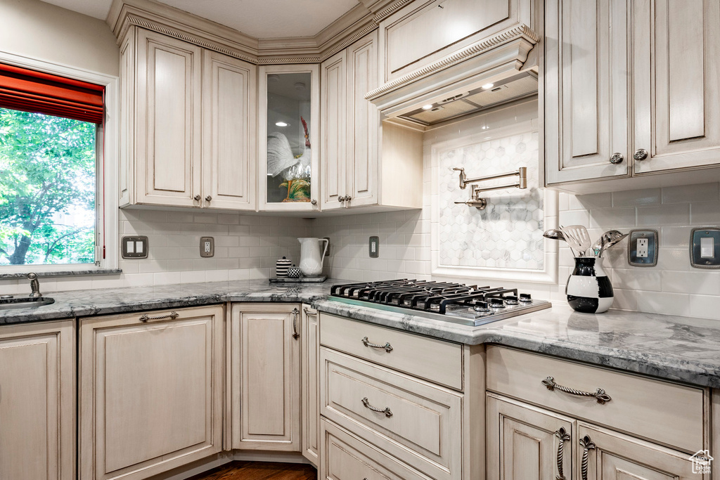 Kitchen featuring stainless steel gas stovetop, decorative backsplash, glass insert cabinets, and light stone countertops