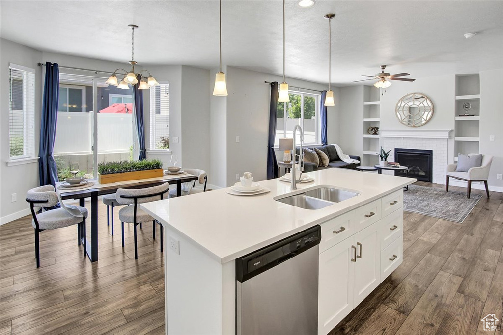 Kitchen with dishwasher, wood finished floors, a brick fireplace, open floor plan, and hanging light fixtures