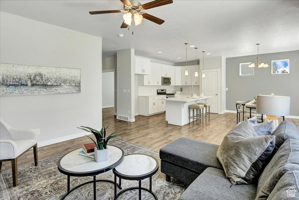 Living room featuring a ceiling fan, light wood-style flooring, a chandelier, and recessed lighting