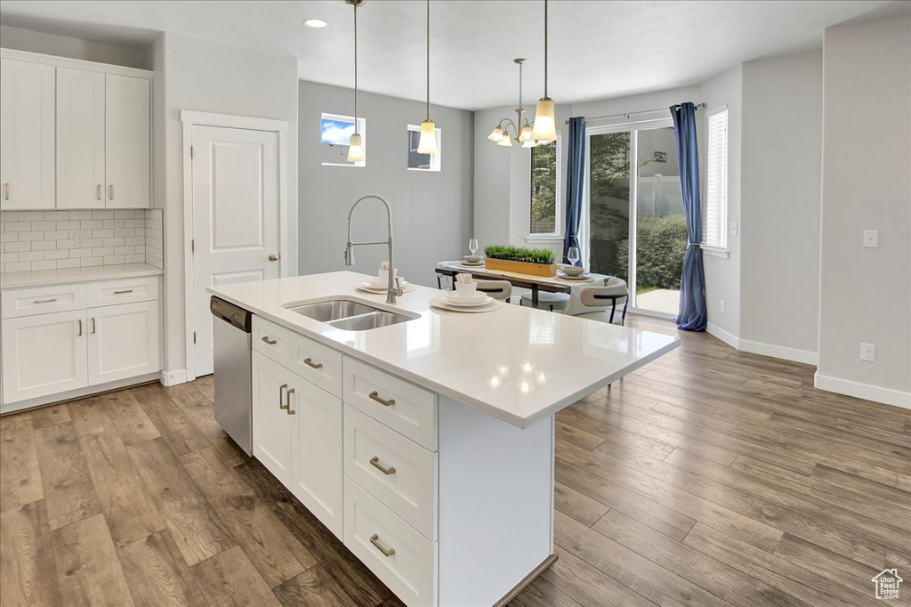 Kitchen featuring stainless steel dishwasher, light countertops, an island with sink, tasteful backsplash, and wood finished floors