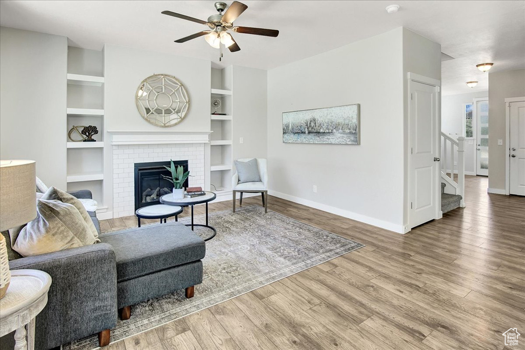 Living area featuring ceiling fan, wood finished floors, stairs, a fireplace, and built in shelves