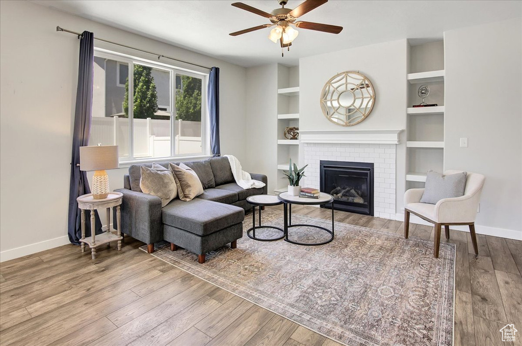 Living area with wood finished floors, a ceiling fan, a brick fireplace, and built in features