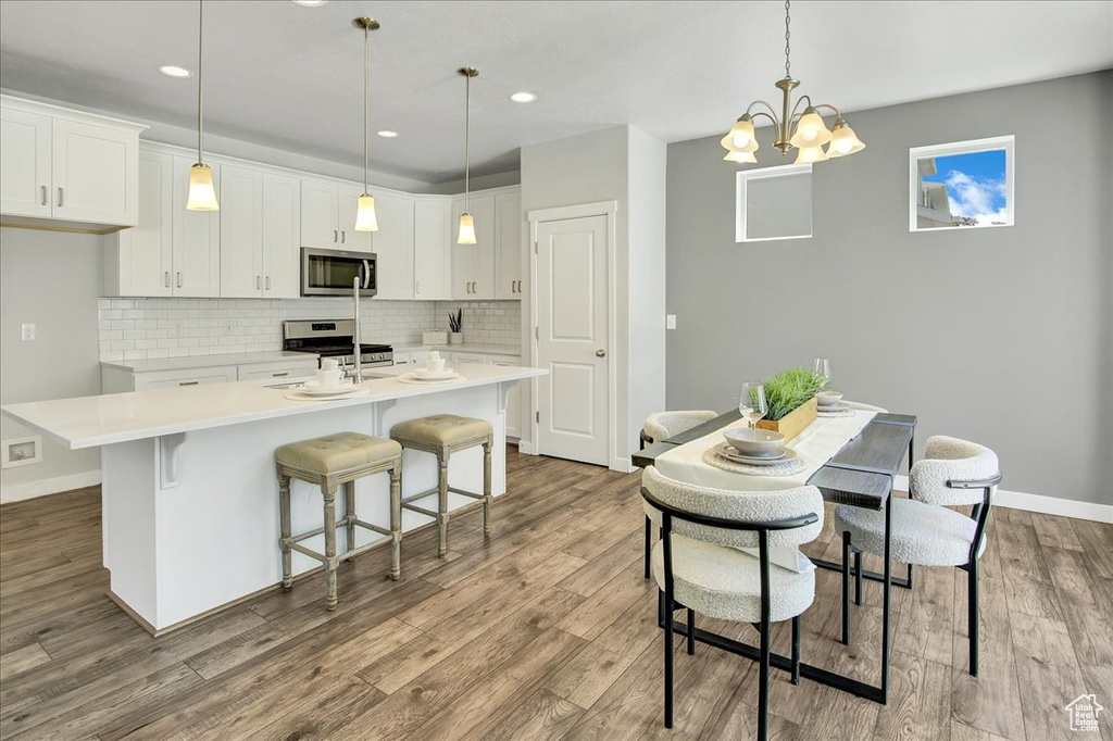 Kitchen with appliances with stainless steel finishes, a kitchen island with sink, wood finished floors, tasteful backsplash, and recessed lighting