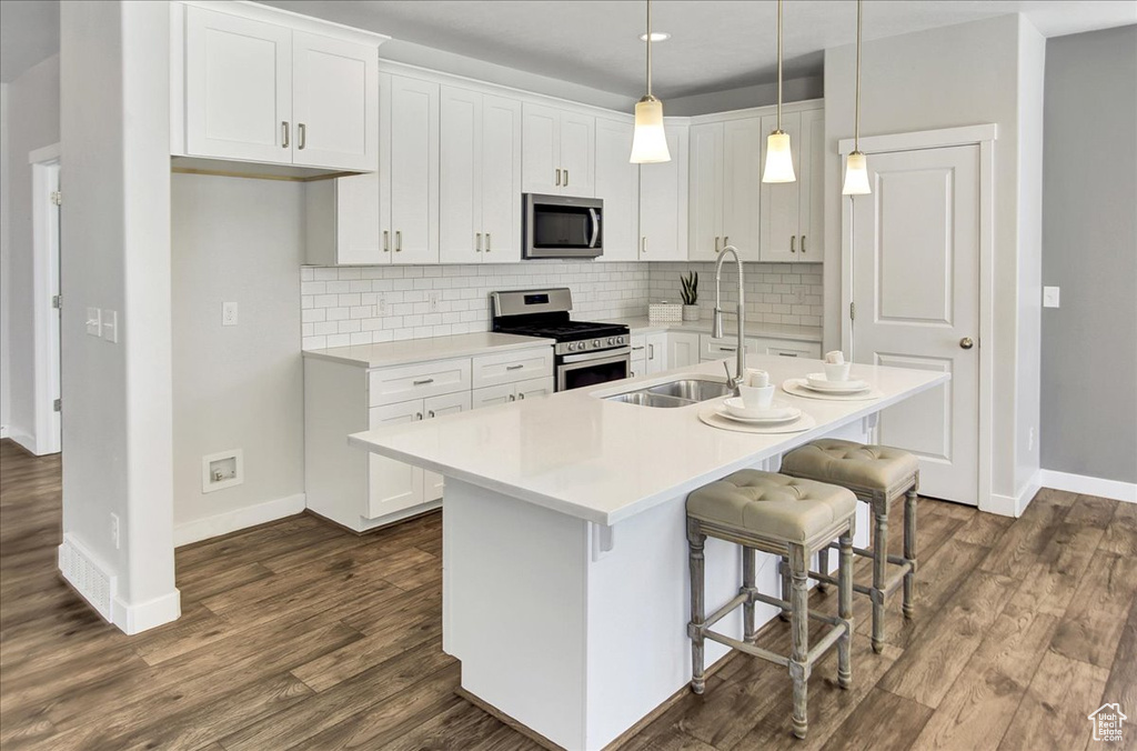 Kitchen featuring appliances with stainless steel finishes, a kitchen island with sink, tasteful backsplash, and dark wood-style flooring