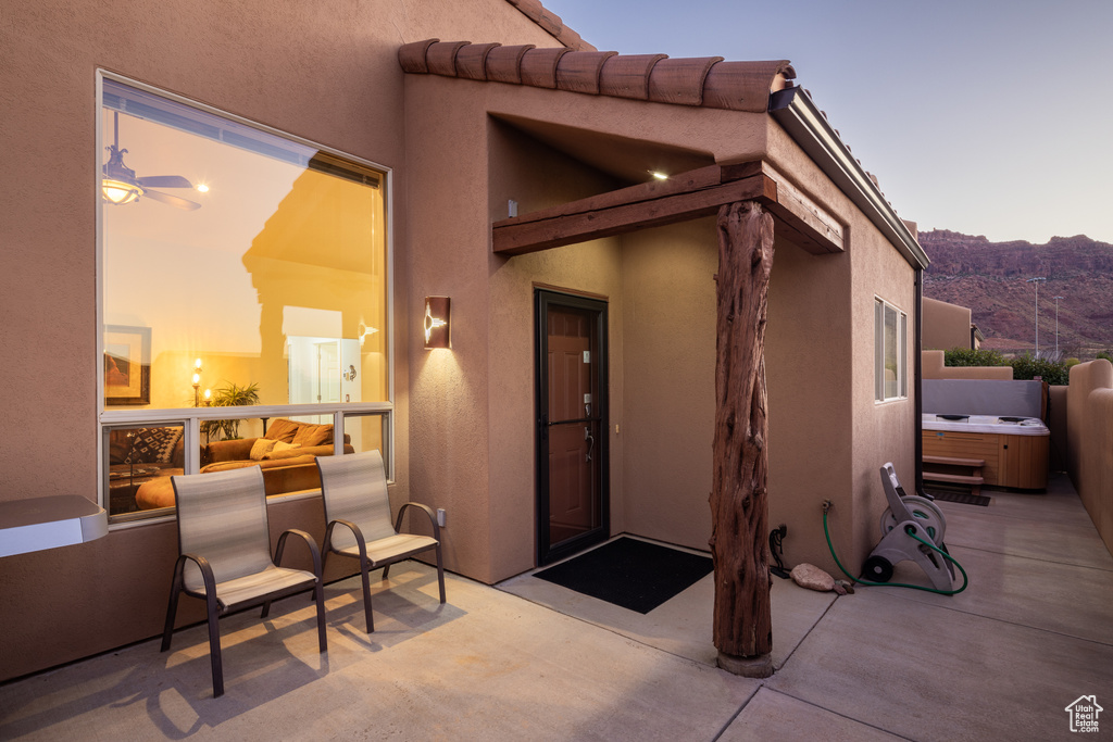 View of exterior entry with a hot tub, a patio, a mountain view, and stucco siding