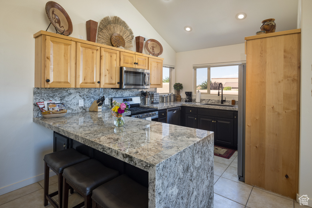 Kitchen with appliances with stainless steel finishes, a peninsula, a breakfast bar area, decorative backsplash, and light tile patterned flooring