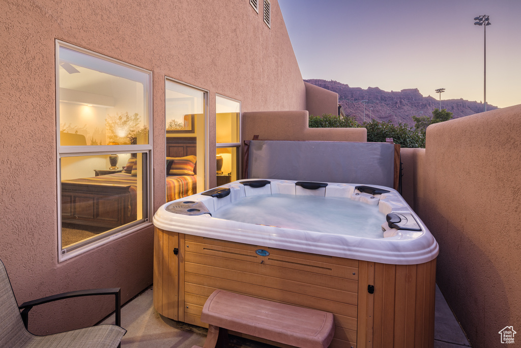 Patio terrace at dusk with a hot tub, a mountain view, and a balcony