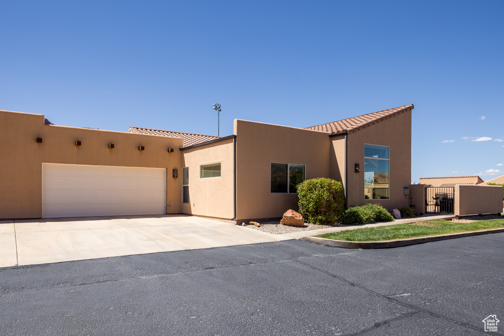 Adobe home with concrete driveway, an attached garage, stucco siding, and a gate