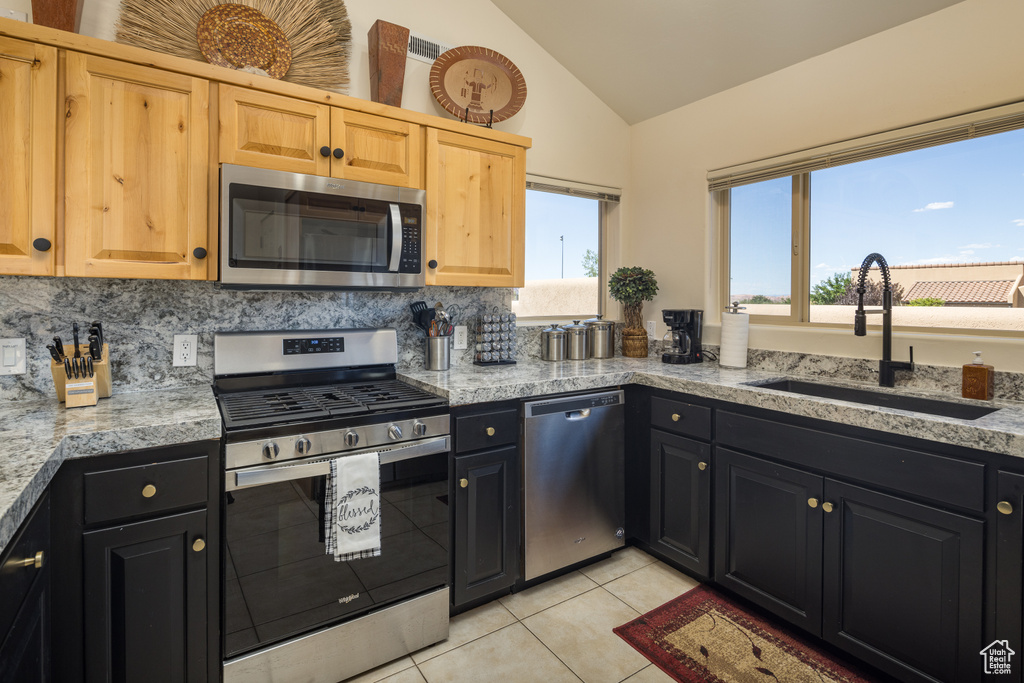 Kitchen featuring appliances with stainless steel finishes, vaulted ceiling, light tile patterned flooring, decorative backsplash, and dark cabinets