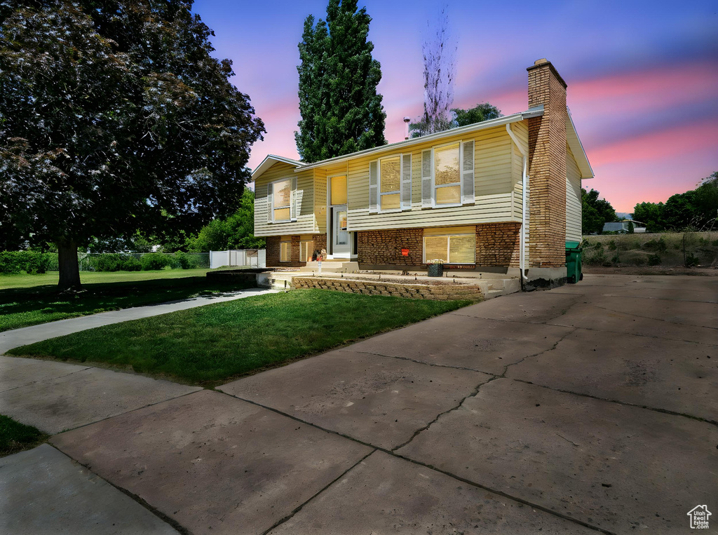 Split foyer home with a front lawn, a chimney, brick siding, and concrete driveway