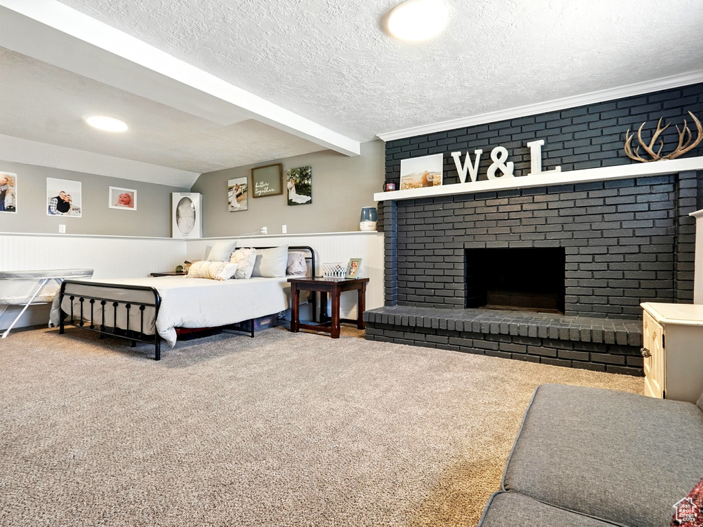 Carpeted bedroom featuring a brick fireplace, a wainscoted wall, and a textured ceiling