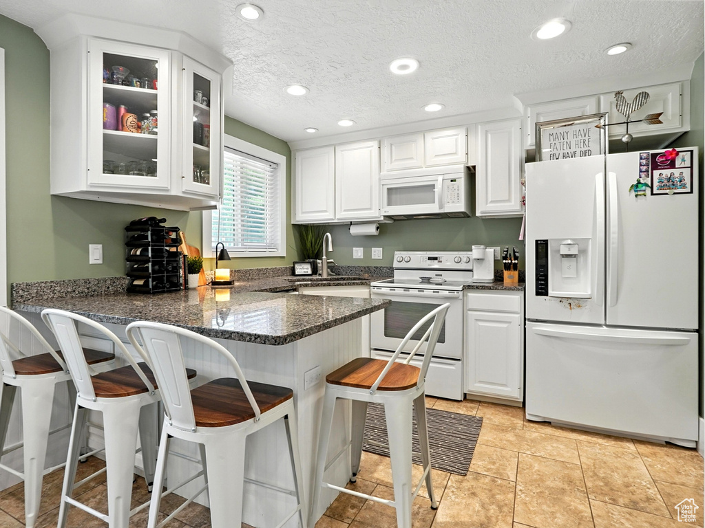 Kitchen with white appliances, a peninsula, white cabinetry, glass insert cabinets, and a breakfast bar area