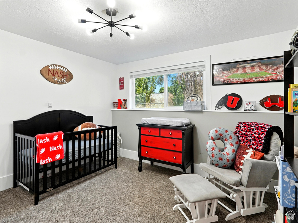Carpeted bedroom with a chandelier, a crib, and a textured ceiling