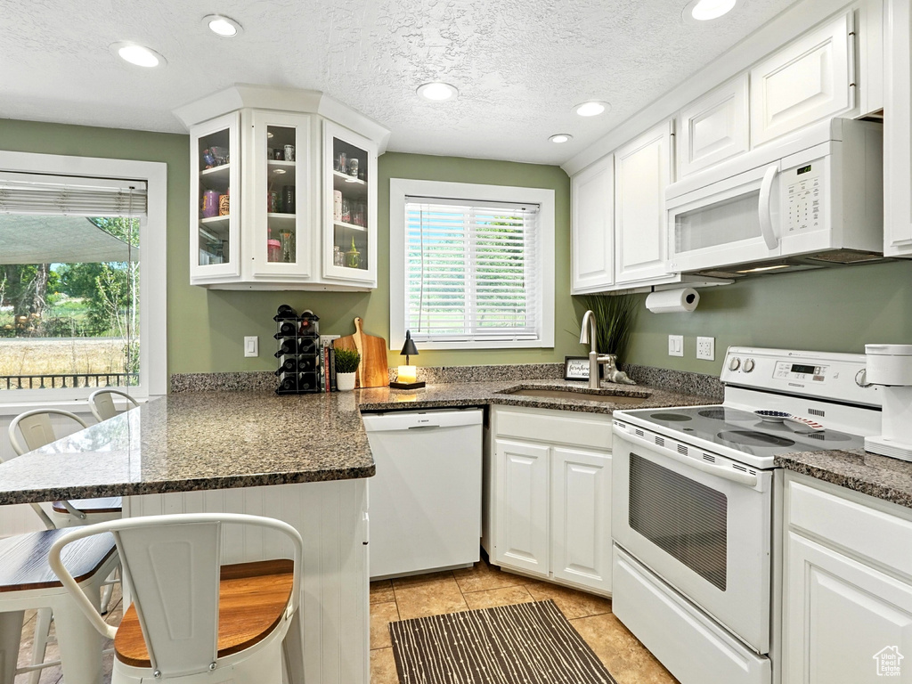 Kitchen with white appliances, a peninsula, white cabinetry, glass insert cabinets, and light tile patterned flooring