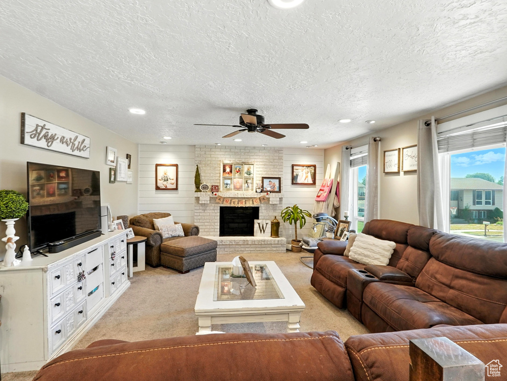 Living area featuring a textured ceiling, a ceiling fan, light colored carpet, a fireplace, and recessed lighting